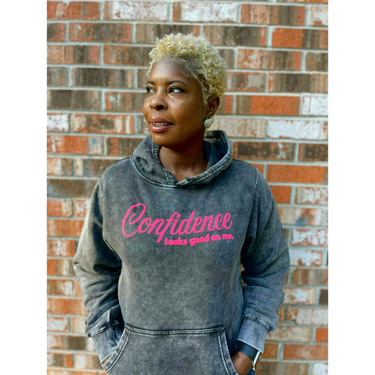 Person wearing a hoodie with 'Confidence looks good on me' text against a brick wall.