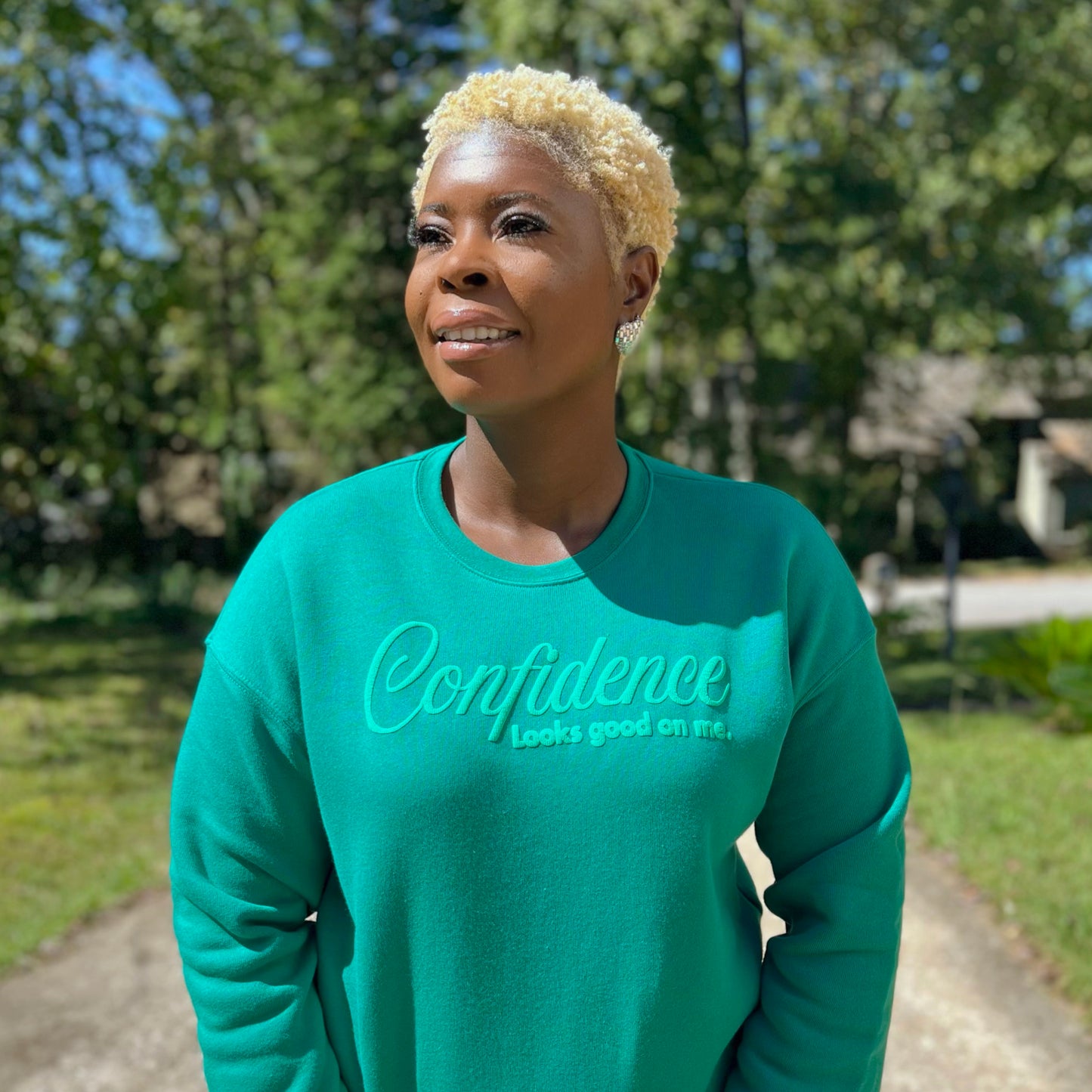 woman wearing a kelly green sweatshirt with 'Confidence looks good on me' text outdoors.