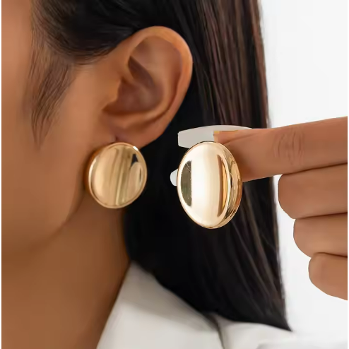 Close-up of woman wearing high-shine gold button stud earrings with a classic oval shape.