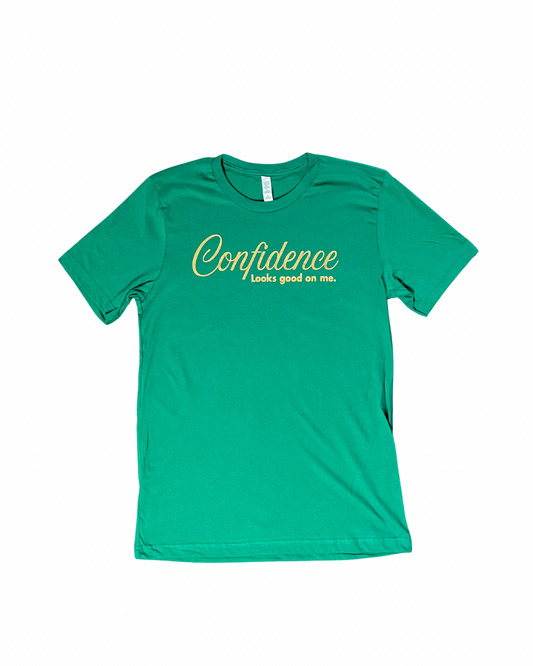 flat lay of kelly green t-shirt with 'Confidence looks good on me' text  in metallic gold, on white background.