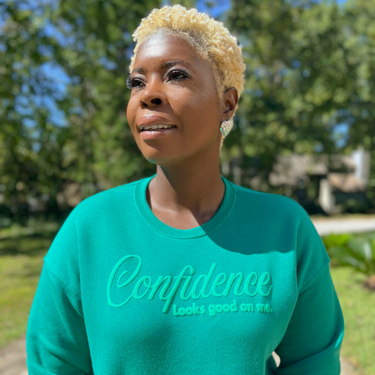 Woman wearing a kelly green sweatshirt with 'Confidence Looks good on me' text outdoors.