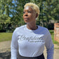 Woman wearing a ash grey long-sleeve shirt with 'Confidence Looks good on me' text in black, outdoors. 