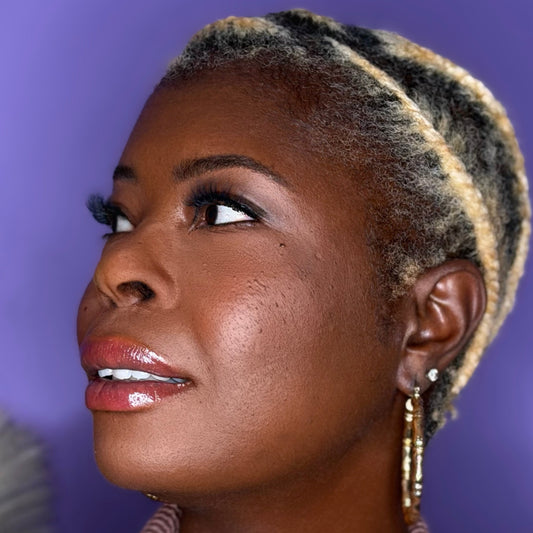 Woman with styled hair against a purple background wearing Nori lashes