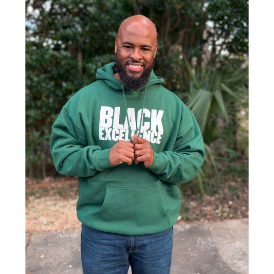 Male wearing a forest green hoodie with “Black Excellence” in bold white puff print.
