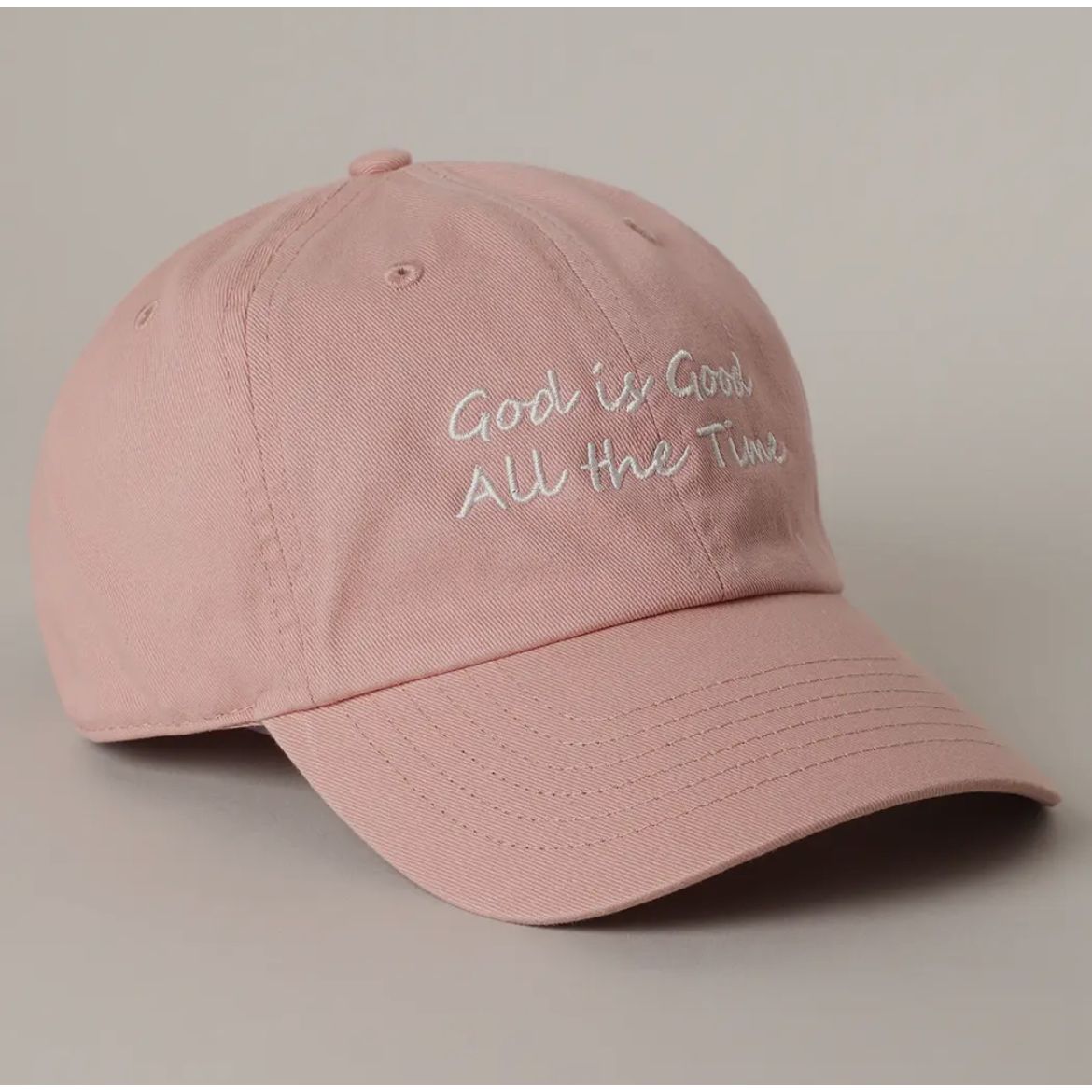 Pink cap with 'God is Good All the Time' text on a beige background
