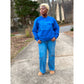 Model wearing a royal blue sweatshirt featuring the “Pray, Manifest, Work, Succeed, Repeat” design in puff print; with light blue denim and tan birkenstocks
