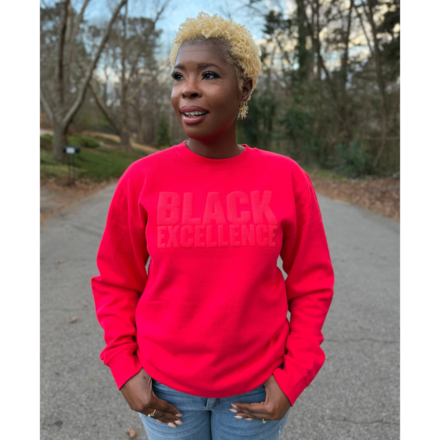 Woman modeling a red sweatshirt featuring the "Black excellence" design in puff print.