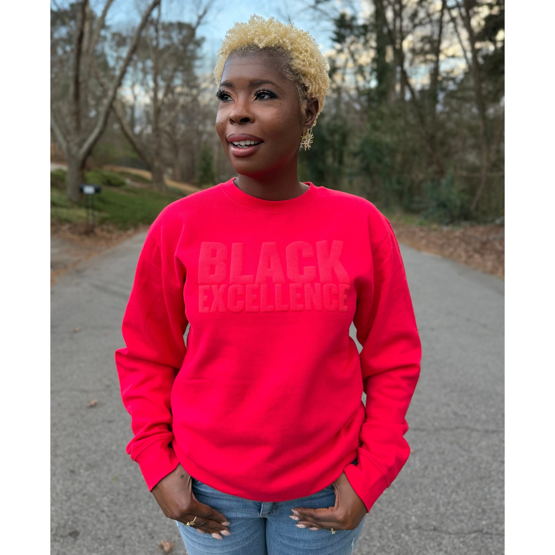Woman modeling a red sweatshirt featuring the "Black excellence" design in puff print.