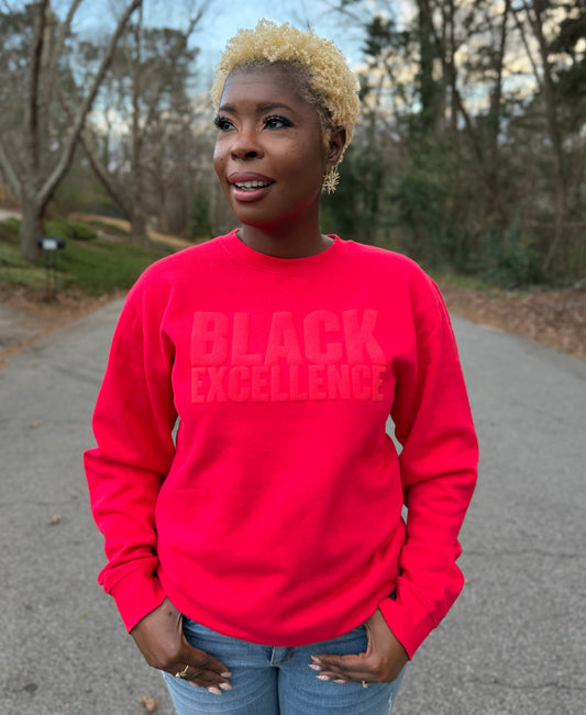 Woman modeling a red sweatshirt featuring the "Black excellence" design in puff print.
