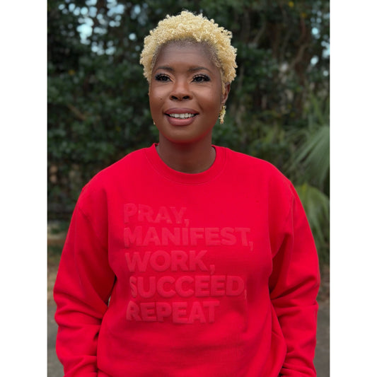 Model wearing a red sweatshirt featuring the “Pray, Manifest, Work, Succeed, Repeat” design in puff print.