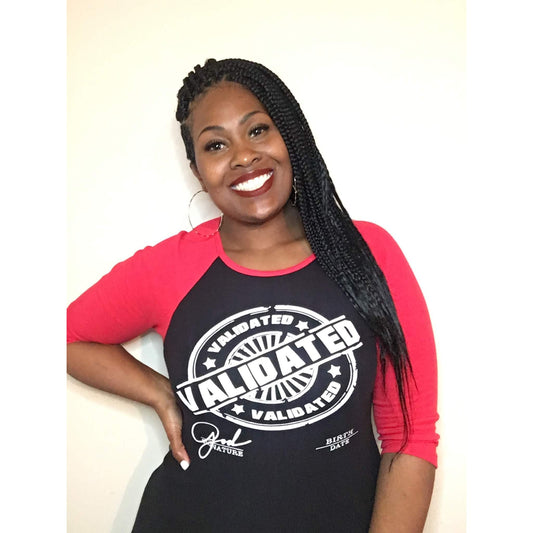 Black woman smiling in a black and red raglan tee featuring the bold white “Validated” stamp design across the chest. Tee has red three-quarter sleeves and a fitted unisex cut.