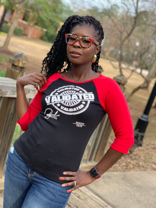 Black woman smiling in a black and red raglan tee featuring the bold white “Validated” stamp design across the chest. Tee has red three-quarter sleeves and a fitted unisex cut.